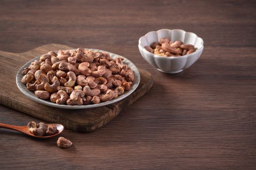 Cashew nuts with peel in a plate on wooden tray and table background, healthy raw food concept.