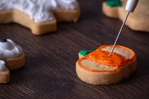 Close up of decorating cute Halloween pumpkin gingerbread cookies with frosting icing cream topping bag.
