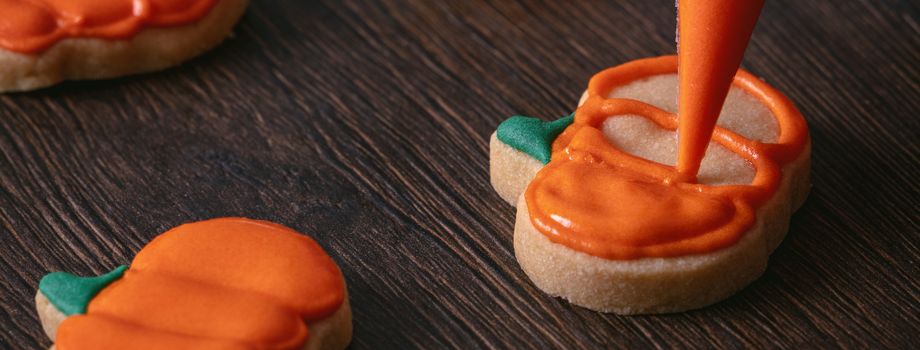 Close up of decorating cute Halloween pumpkin gingerbread cookies with frosting icing cream topping bag.