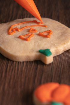 Close up of decorating cute Halloween pumpkin gingerbread cookies with frosting icing cream topping bag.