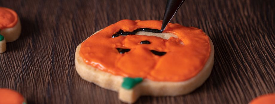 Close up of decorating cute Halloween pumpkin gingerbread cookies with frosting icing cream topping bag.