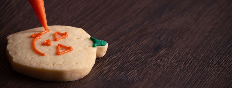 Close up of decorating cute Halloween pumpkin gingerbread cookies with frosting icing cream topping bag.