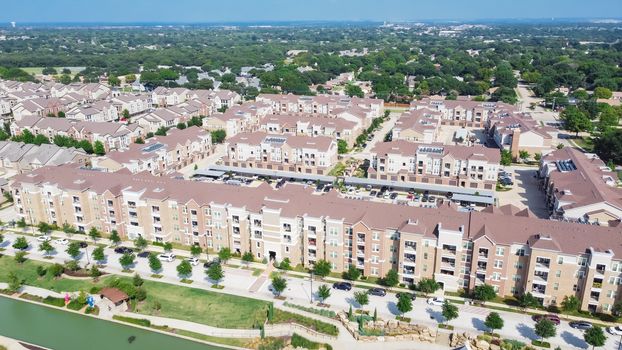Brand new multistory apartment complex with covered parking lots and suburban residential area in background. Master-planned community and census-designated sprawl in Flower Mound, TX