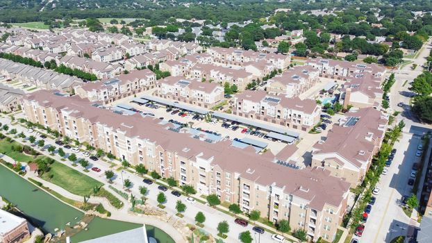 Brand new multistory apartment complex with covered parking lots and suburban residential area in background. Master-planned community and census-designated sprawl in Flower Mound, TX