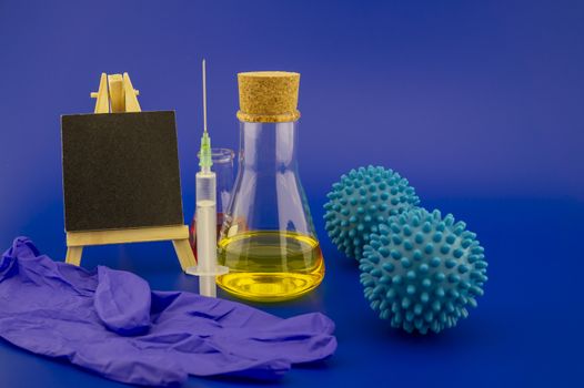 Virus pandemic and possible vaccine concept with surgical mask, hypodermic syringe, pharmaceutical bottle small chalk board and blue virus molecules in blue toned theme with with copy space