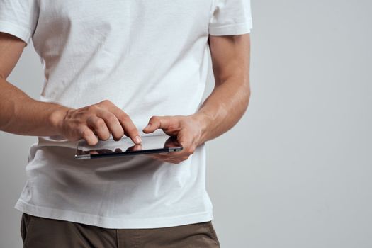 Tablet with a touch screen on a light background male hands white t-shirt cropped view. High quality photo