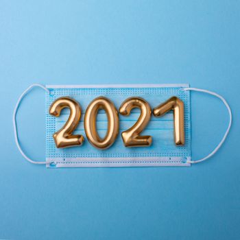 Gold numbers 2021 with face mask on blue background. Happy new pandemic year