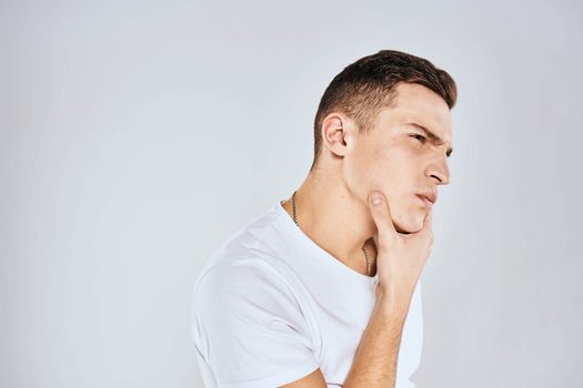 Emotional man in a white t-shirt holds his hand on his face light background. High quality photo