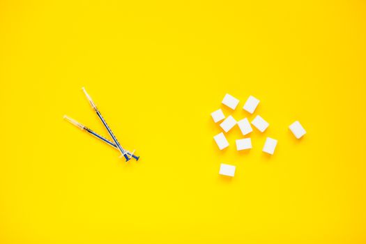Compressed sugar cubes and insulin syringes on a yellow background. Diabetes.