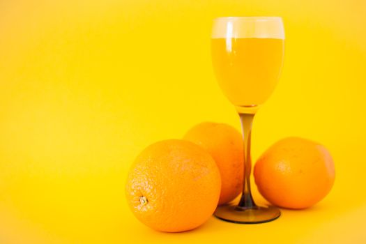 Bright oranges and a glass of orange juice on a bright yellow background. Healthy lifestyle concept. Vitamins and vigor.