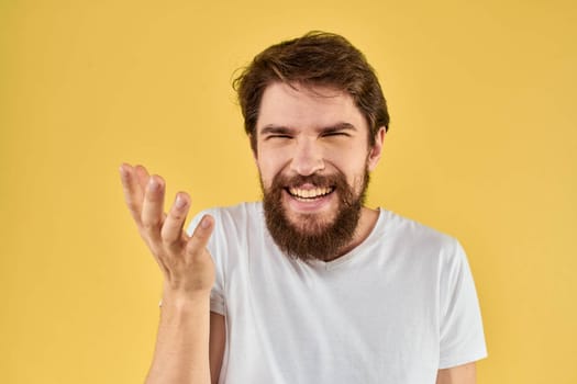 Bearded man emotions fun gesture with hands white t-shirt close-up yellow background. High quality photo