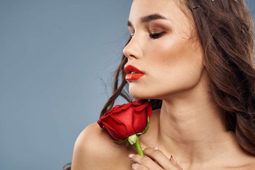 Woman portrait with red rose near the face on gray background and makeup curly hair. High quality photo