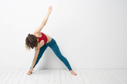 sports woman in a bright room doing yoga in full growth blue leggings and a red tank top. High quality photo