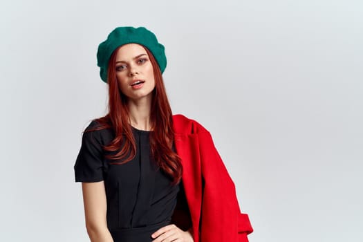 A woman holds in her hand a red coat and a dark T-shirt Green hat cropped view of a light background. High quality photo