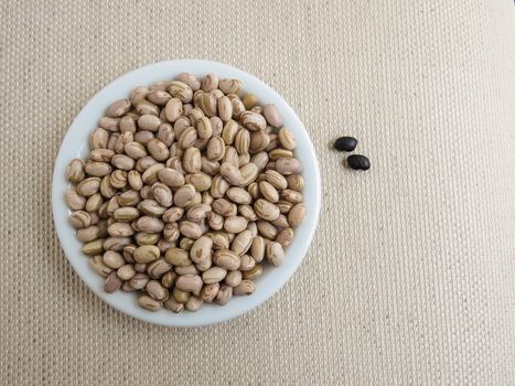 Handful of Rio beans on a white plate and isolated black beans, top view.