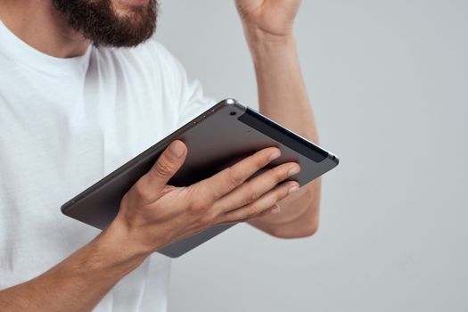 Tablet with a touch screen on a light background male hands white t-shirt cropped view. High quality photo