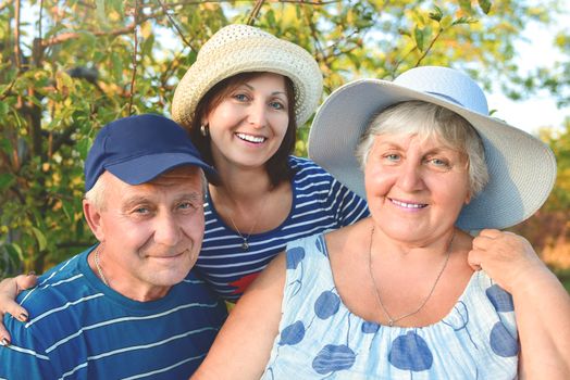 Beautiful senior couple is sitting on the bench in the park with their adult daughter. Grandma and grandpa are hugging and smiling. Real love and family relationship photo. Generations concept.