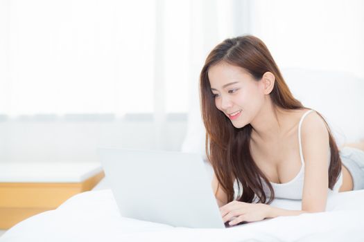 Beautiful asian young woman lying on bed using laptop at bedroom for leisure and relax, freelance with girl working notebook, communication concept.