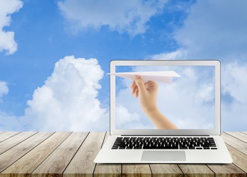 Hand with paper plane with laptop on wood table against blue sky sending email, communication concept. 