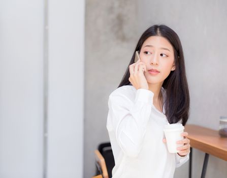 Beautiful young asian woman talking phone and smile in the coffee shop, businesswoman sitting in cafe free time, freelancer female calling telephone, communication concept.