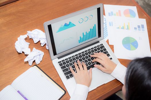 Businesswoman tired and stressed with overworked at desk, girl with worried not idea with graph analysis laptop and crumpled paper at office, business concept.