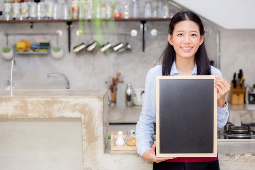 Portrait of beautiful young barista, asian woman is a employee standing holding chalkboard in counter coffee shop, service concept.