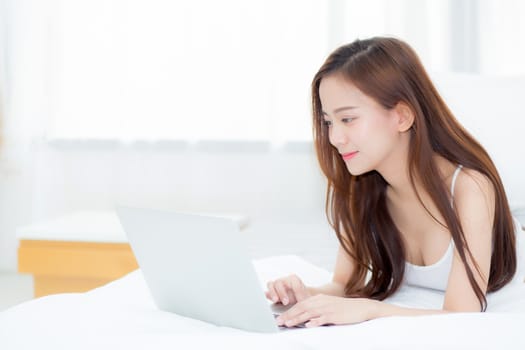 Beautiful asian young woman lying on bed using laptop at bedroom for leisure and relax, freelance with girl working notebook, communication concept.