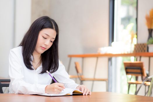 Beautiful business asian young woman writing on notebook on table, girl work at coffee shop, freelance business concept.