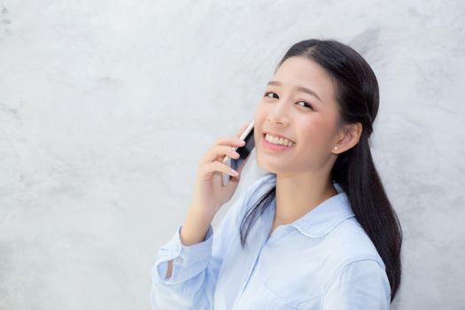 Beautiful young asian woman talking phone and smile standing on cement background, freelancer female calling telephone, communication concept.