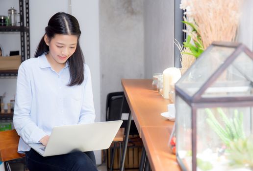 Beautiful asian young woman working online on laptop sitting at coffee shop, professional female freelancer using notebook computer with connect to internet for distance job.