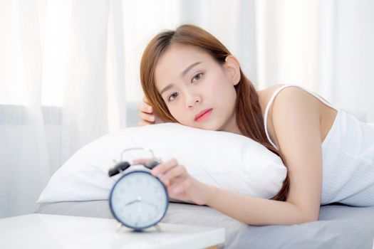 Beautiful asian young woman turn off alarm clock in morning, wake up for sleep with alarm clock, relax and lifestyle concept.