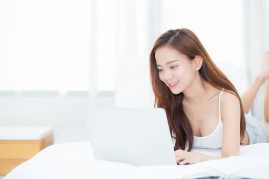 Beautiful asian young woman lying on bed using laptop at bedroom for leisure and relax, freelance with girl working notebook, communication concept.