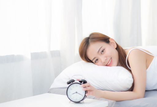 Beautiful asian young woman turn off alarm clock in morning, wake up for sleep with alarm clock, relax and lifestyle concept.