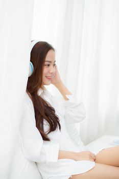 Beautiful asian young woman enjoy listen music with headphone while sitting in bedroom, relax girl with earphone internet online, leisure and technology concept.