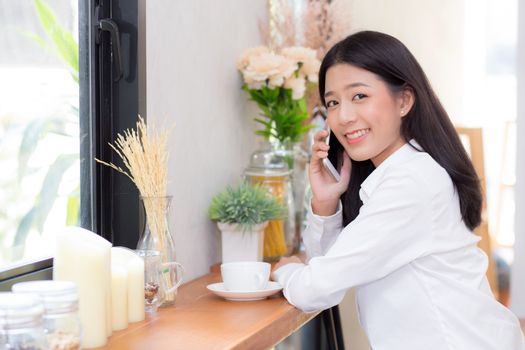 Beautiful young asian woman talking phone and smile in the coffee shop, businesswoman sitting in cafe free time, freelancer female calling telephone, communication concept.