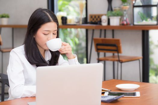 Beautiful asian young woman working online on laptop and drink coffee sitting at coffee shop, professional female freelancer using notebook computer with connect to internet for distance job.