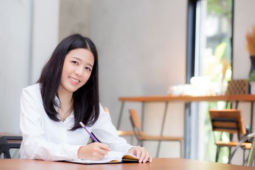 Beautiful business asian young woman writing on notebook on table, girl work at coffee shop, freelance business concept.