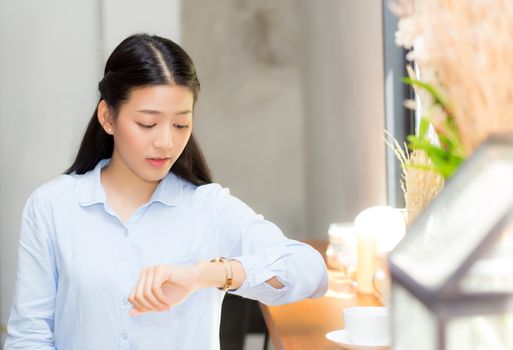 Beautiful asian young woman look at watch waiting for friend or someone, girl checking clock with appointment at coffee shop.