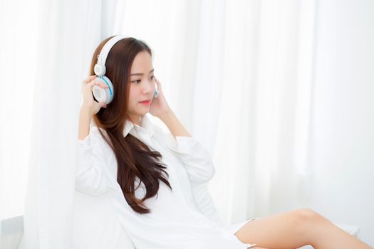 Beautiful asian young woman enjoy listen music with headphone while sitting in bedroom, relax girl with earphone internet online, leisure and technology concept.