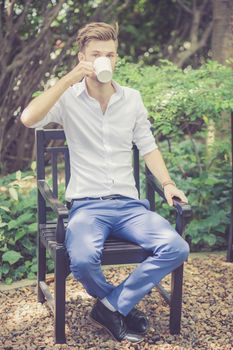 Portrait business young handsome man drink cup of coffee sitting in the park, relax and leisure concept.