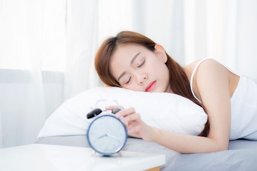 Beautiful asian young woman turn off alarm clock in morning, wake up for sleep with alarm clock, relax and lifestyle concept.