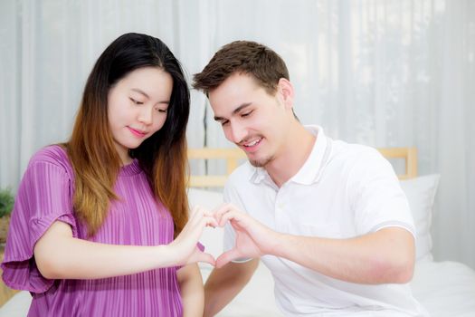 Pregnant Mother and father sitting geture hand heart shape with hand in bedroom, happy family concept.