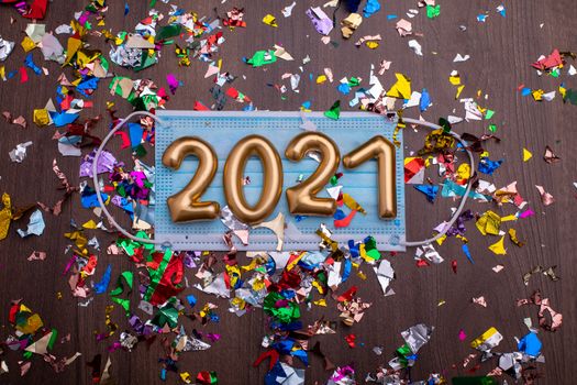 Gold numbers 2021 on face mask and confetti. Happy new pandemic year
