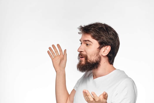 cheerful bearded man in a white t-shirt emotions gestures with his hands light background studio. High quality photo