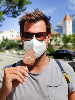 Young guy on summer vacations wearing corona virus protective face mask not beeing able to lick ice cream bar.
