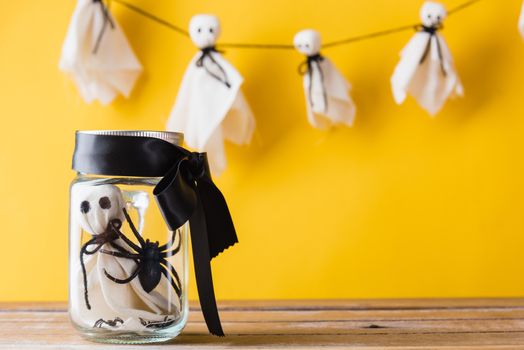 Funny Halloween day decoration party, Cute white ghost crafts scary face hanging on background have only one baby ghost in jar glass, isolated yellow, Happy holiday DIY handicraft concept