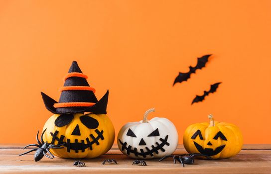 Funny Halloween day decoration party, Cute pumpkin ghost scary jack o lantern face, black spider and bats on wooden table, studio shot isolated on an orange background, Happy holiday concept