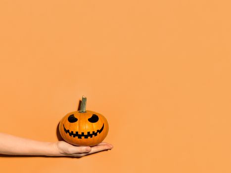 Halloween pumpkin in hand on orange background. Halloween concept with copy space for text or design. Hard light. Jack-o-lantern laughing face on orange squash