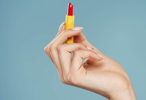 Woman holding lipstick in hand on blue background cropped view of model. High quality photo