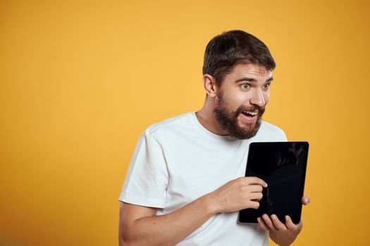 Man with a tablet on a yellow background in a white t-shirt new technologies businessman touch screen touchpad. High quality photo